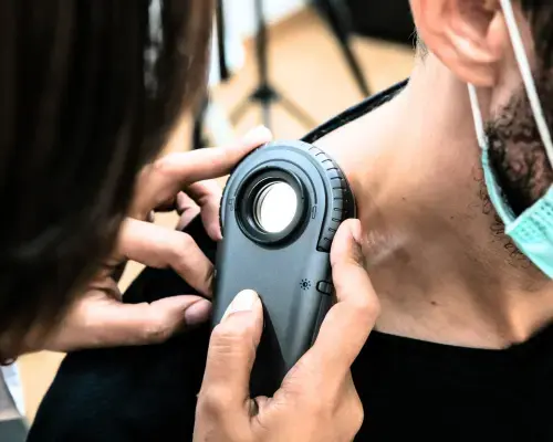 Doctor using a dermatoscope to check a lesion on a patient's arm